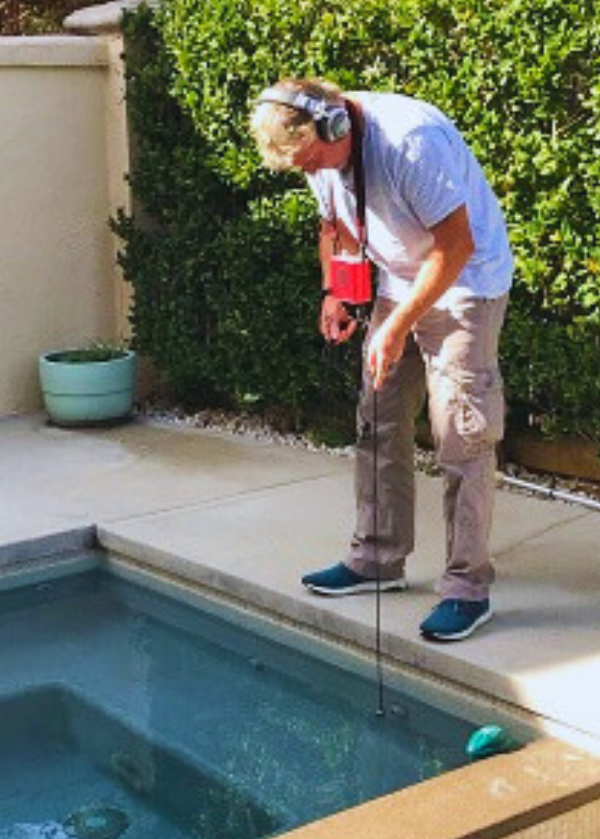 man bending over pool using hydrophone technology to detect pool leak